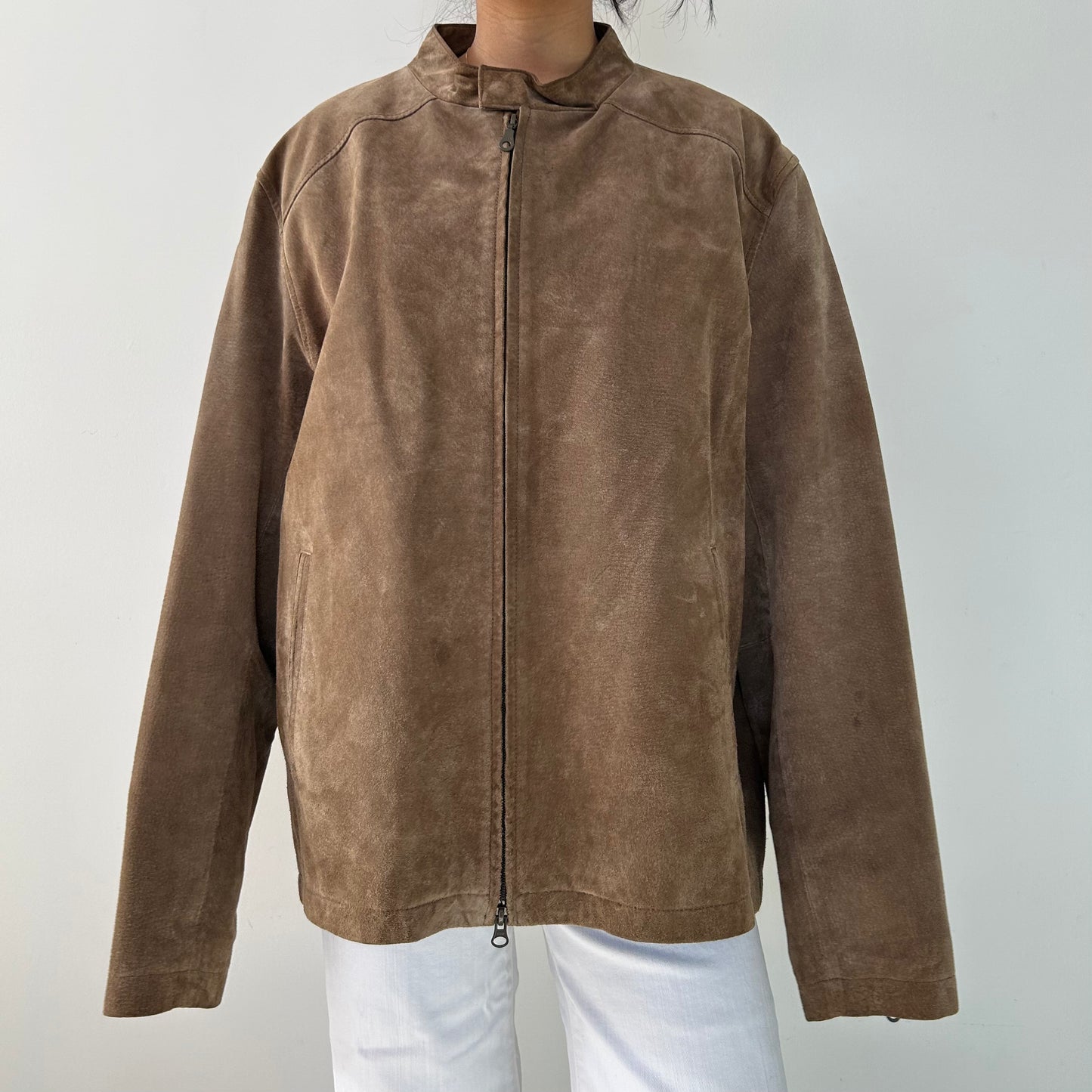 A brown leather jacket with a collared neckline, zippered front, and a zippered chest pocket, worn by a person against a white background.