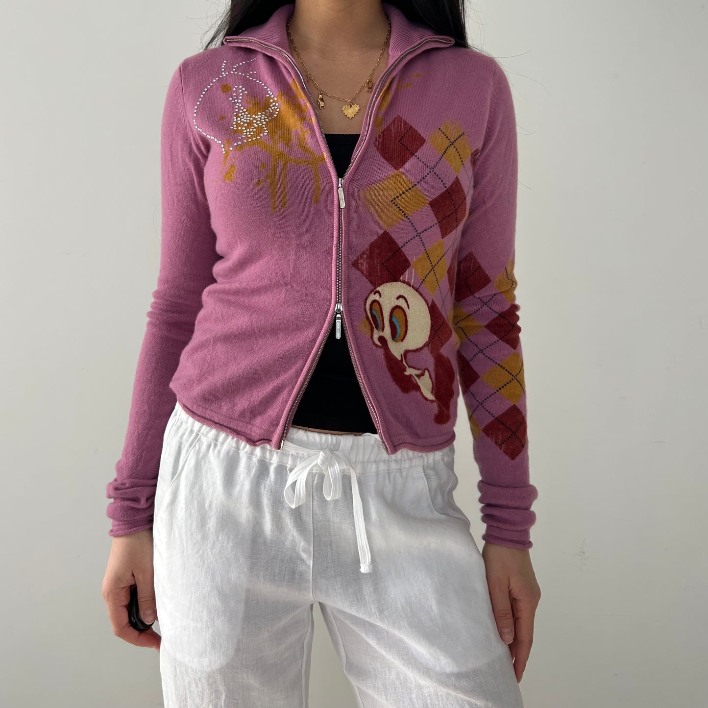 A pink double zip cashmere knit cardigan with an argyle pattern and a Tweety Bird graphic on the front, featuring a high collar and ribbed cuffs.