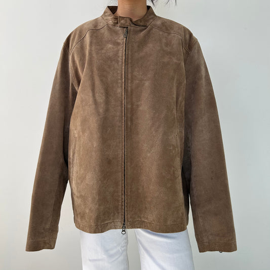 A brown leather jacket with a collared neckline, zippered front, and a zippered chest pocket, worn by a person against a white background.